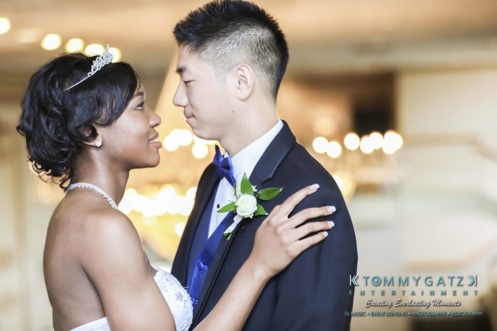 A bride and groom gaze at each other, with the bride wearing a tiara and holding the groom's lapel. The groom wears a suit and boutonniere.