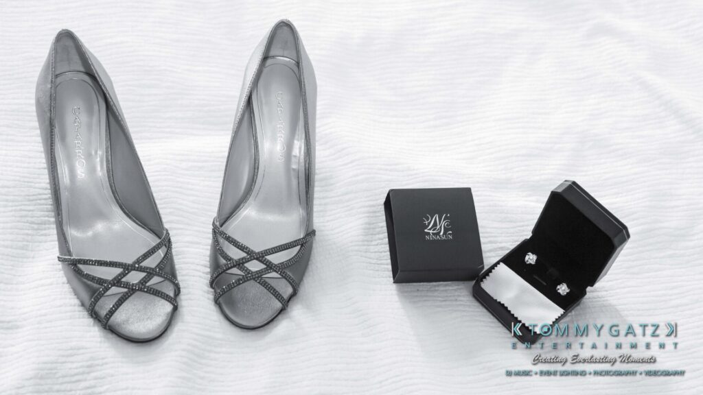 Silver high-heeled shoes next to an open jewelry box displaying earrings and a matching closed box on a white textured surface.