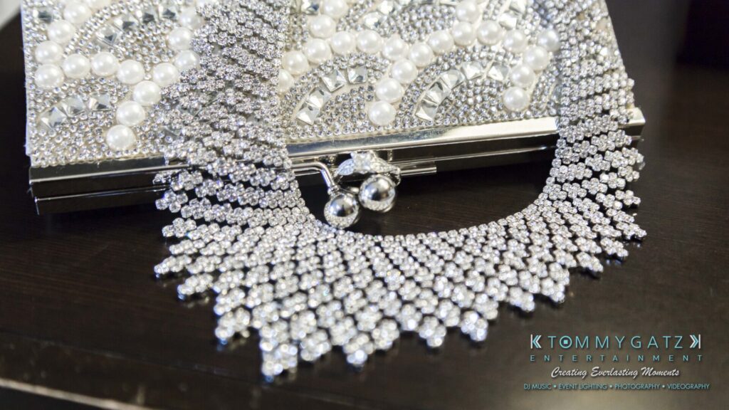 A silver, rhinestone-encrusted necklace and matching earrings are displayed on a sparkling clutch adorned with pearls and sequins.