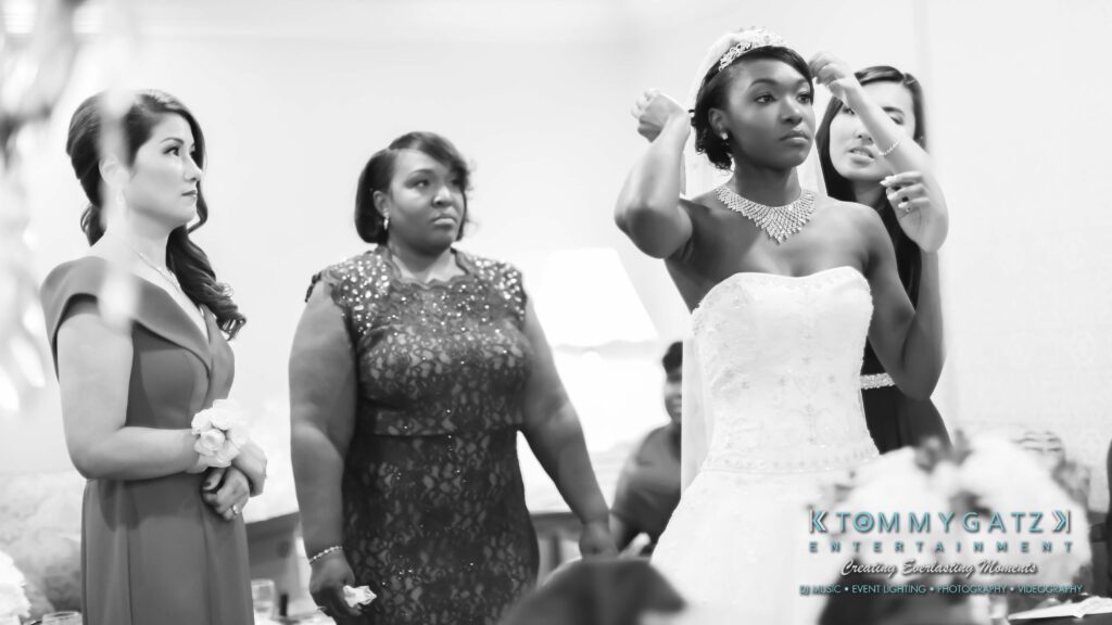Bride adjusting her tiara while surrounded by three women, two standing and one assisting, in a room with a sofa in the background.