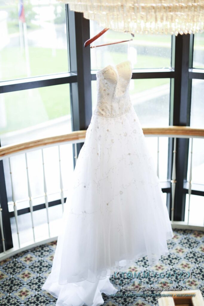 A white wedding dress with a strapless bodice and beaded details hangs in front of a window on a spiral staircase.