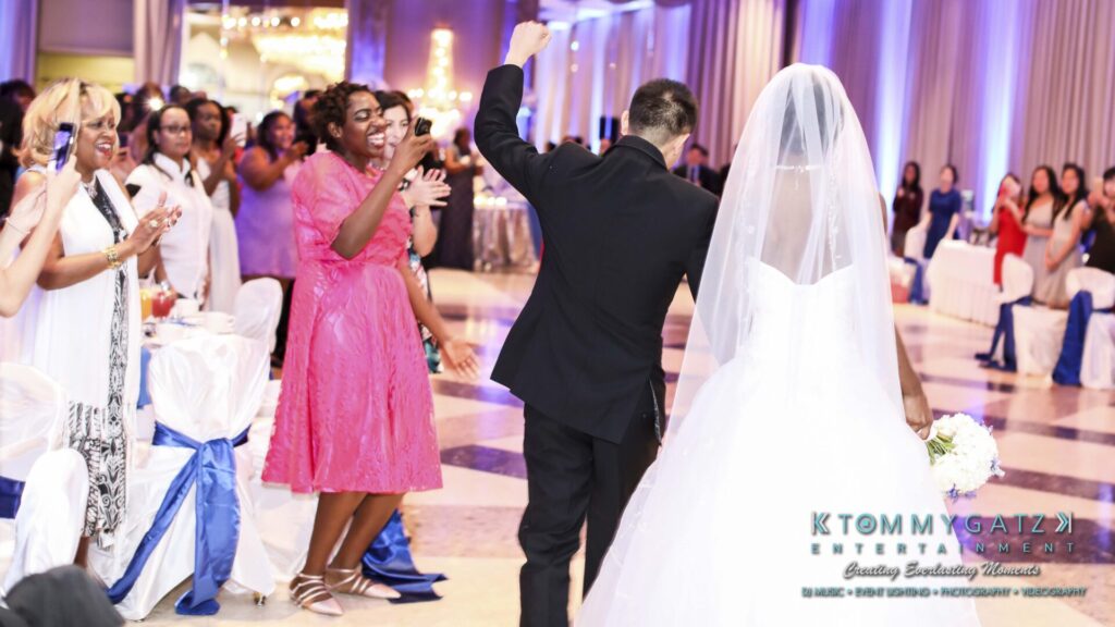 Bride and groom walking into a wedding reception hall as guests applaud and cheer.