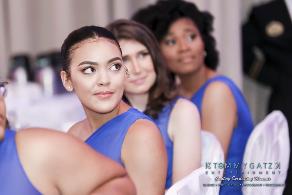 A group of women in blue dresses seated at an event, with one woman in the foreground looking to the side.
