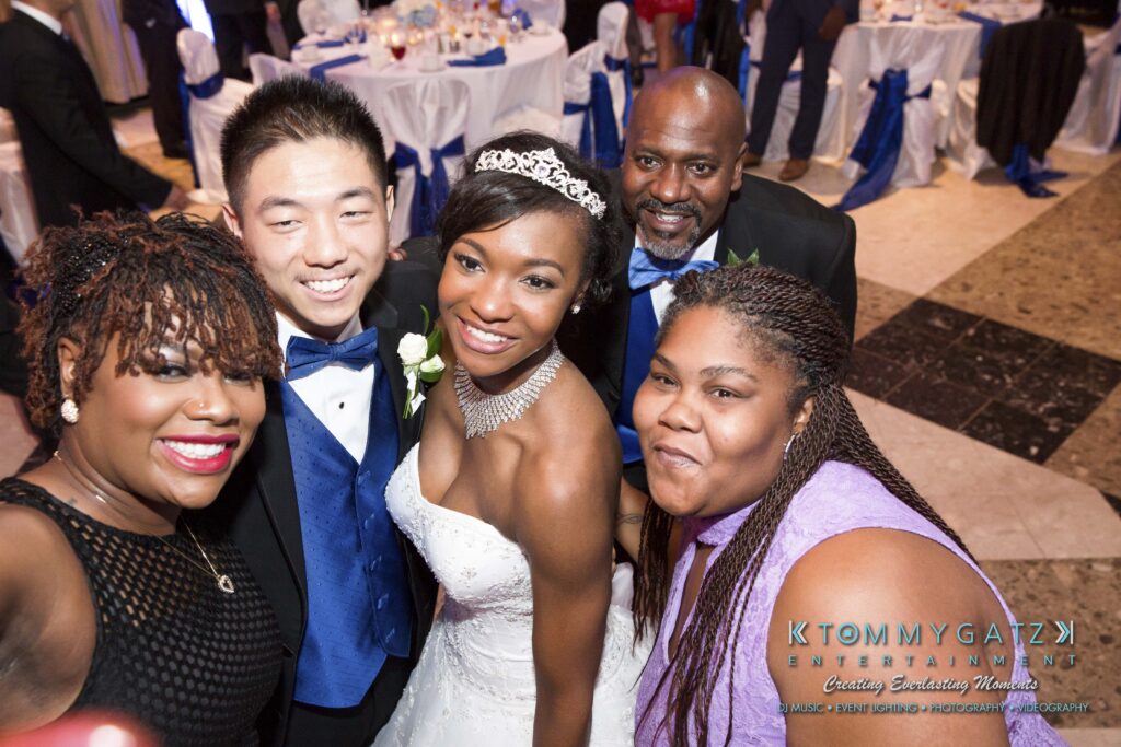 Five people smiling for a group photo at a wedding reception, with a bride in a white dress and tiara in the center.