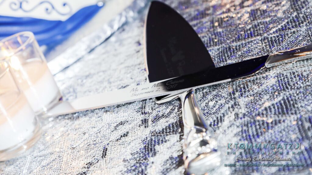 Close-up of a cake knife and server with decorative handles resting on a textured surface, next to three lit votive candles.