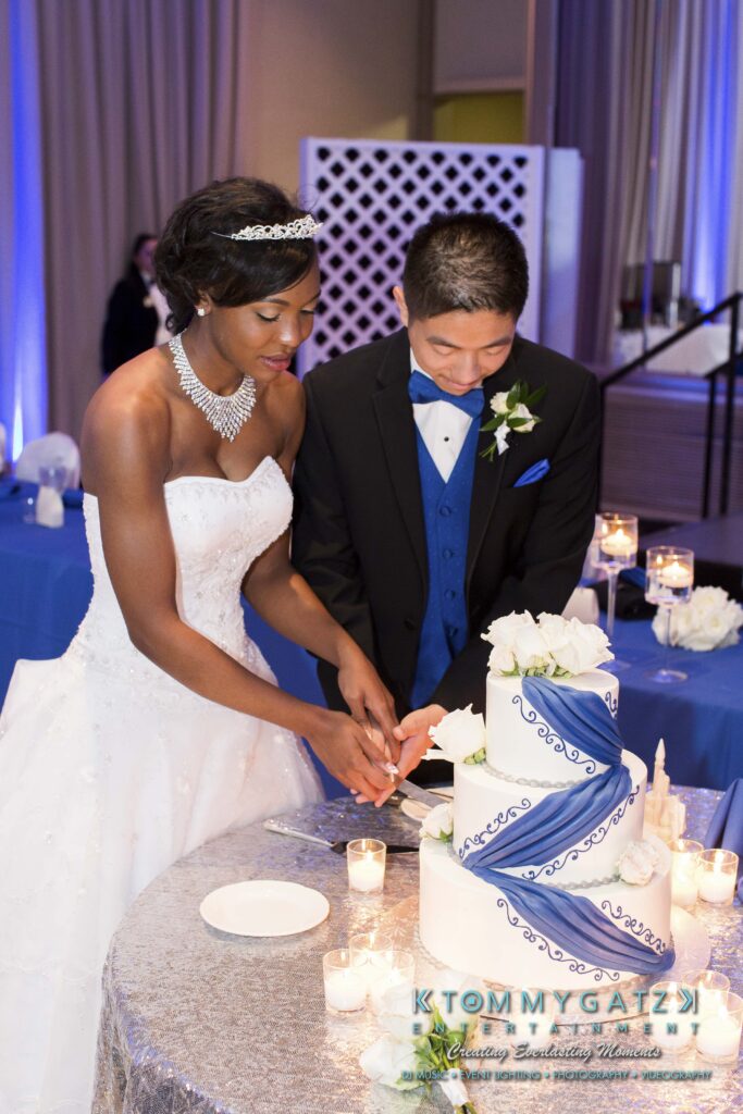 Bride and groom cutting a tiered wedding cake decorated with blue and white ribbons and white roses.