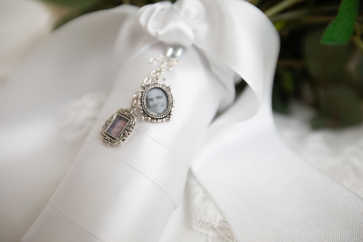 Scarlett-Michael-Wedding-Low-Res-12 - TOMMY GATZ ENTERTAINMENT Close-up of a white ribbon with two small vintage photo charms attached, featuring black-and-white portraits. The ribbon is tied around what appears to be a bouquet.