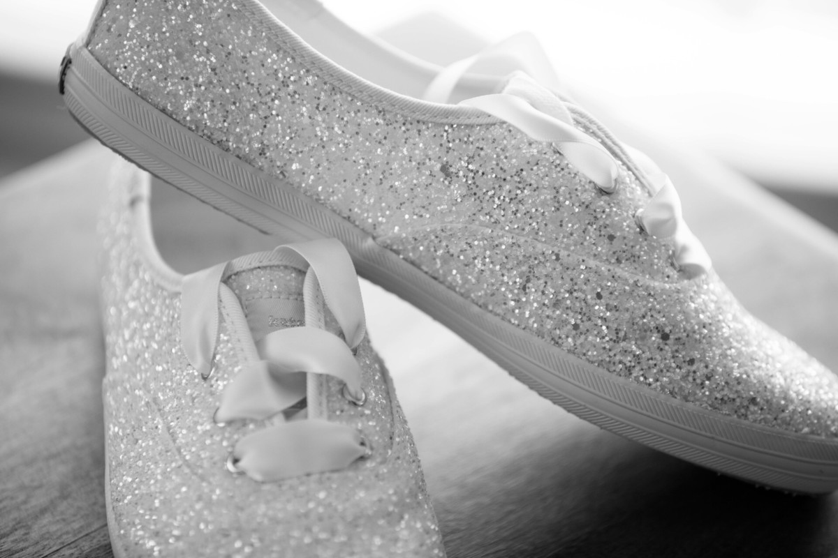Scarlett-Michael-Wedding-Low-Res-16 - TOMMY GATZ ENTERTAINMENT Black and white image of glittery sneakers with ribbon laces resting on a wooden surface.