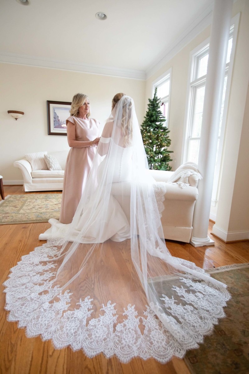 Scarlett-Michael-Wedding-Low-Res-37 - TOMMY GATZ ENTERTAINMENT A bride in a white gown and veil sits with a woman in a pink dress in a living room. A decorated Christmas tree is visible in the background.