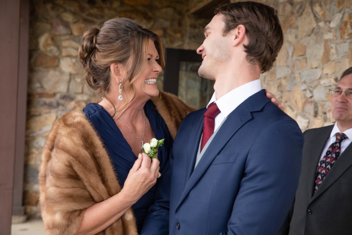 Scarlett-Michael-Wedding-Low-Res-40 - TOMMY GATZ ENTERTAINMENT A woman in a fur stole laughs with a man in a blue suit. Another man in a suit stands nearby. They're outside near a stone wall.