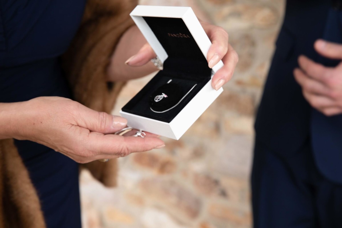 Scarlett-Michael-Wedding-Low-Res-42 - TOMMY GATZ ENTERTAINMENT Person holding an open jewelry box displaying a necklace inside. Another person stands nearby.