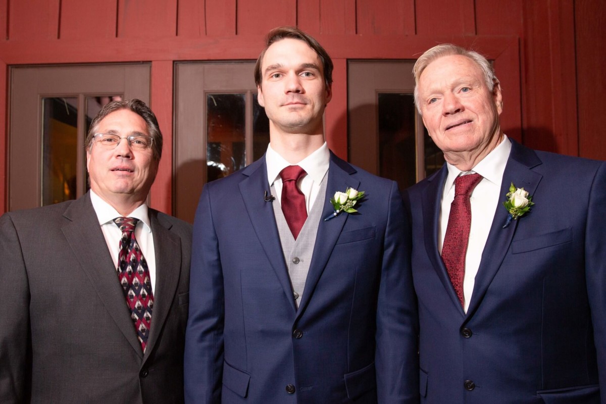 Scarlett-Michael-Wedding-Low-Res-53 - TOMMY GATZ ENTERTAINMENT Three men in suits with boutonnières stand in front of a wooden door, posed for a formal photo.