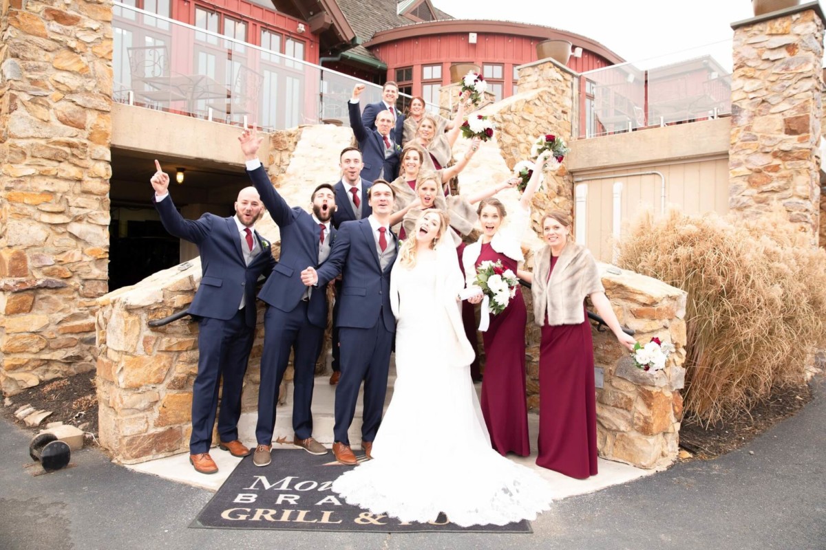 Scarlett-Michael-Wedding-Low-Res-62 - TOMMY GATZ ENTERTAINMENT A bride and groom celebrate with their wedding party on stone steps. The group is dressed in formal attire, with several people holding bouquets.