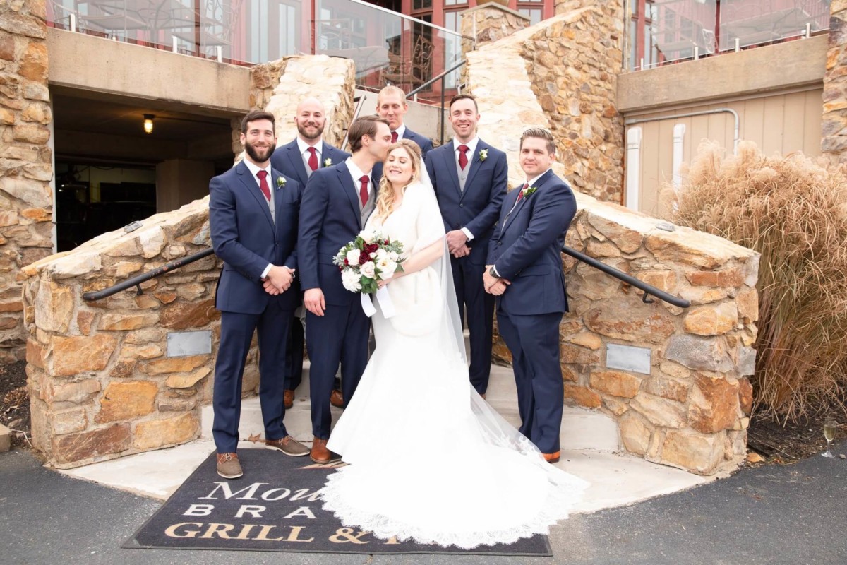 Scarlett-Michael-Wedding-Low-Res-64 - TOMMY GATZ ENTERTAINMENT A bride and six groomsmen in formal attire pose on stone steps outside a building.