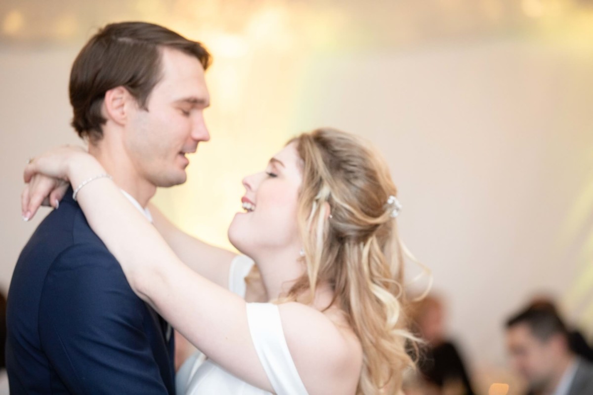 Scarlett-Michael-Wedding-Low-Res-77 - TOMMY GATZ ENTERTAINMENT A couple dancing closely, with the woman smiling and holding the man around the neck, in a softly lit room.