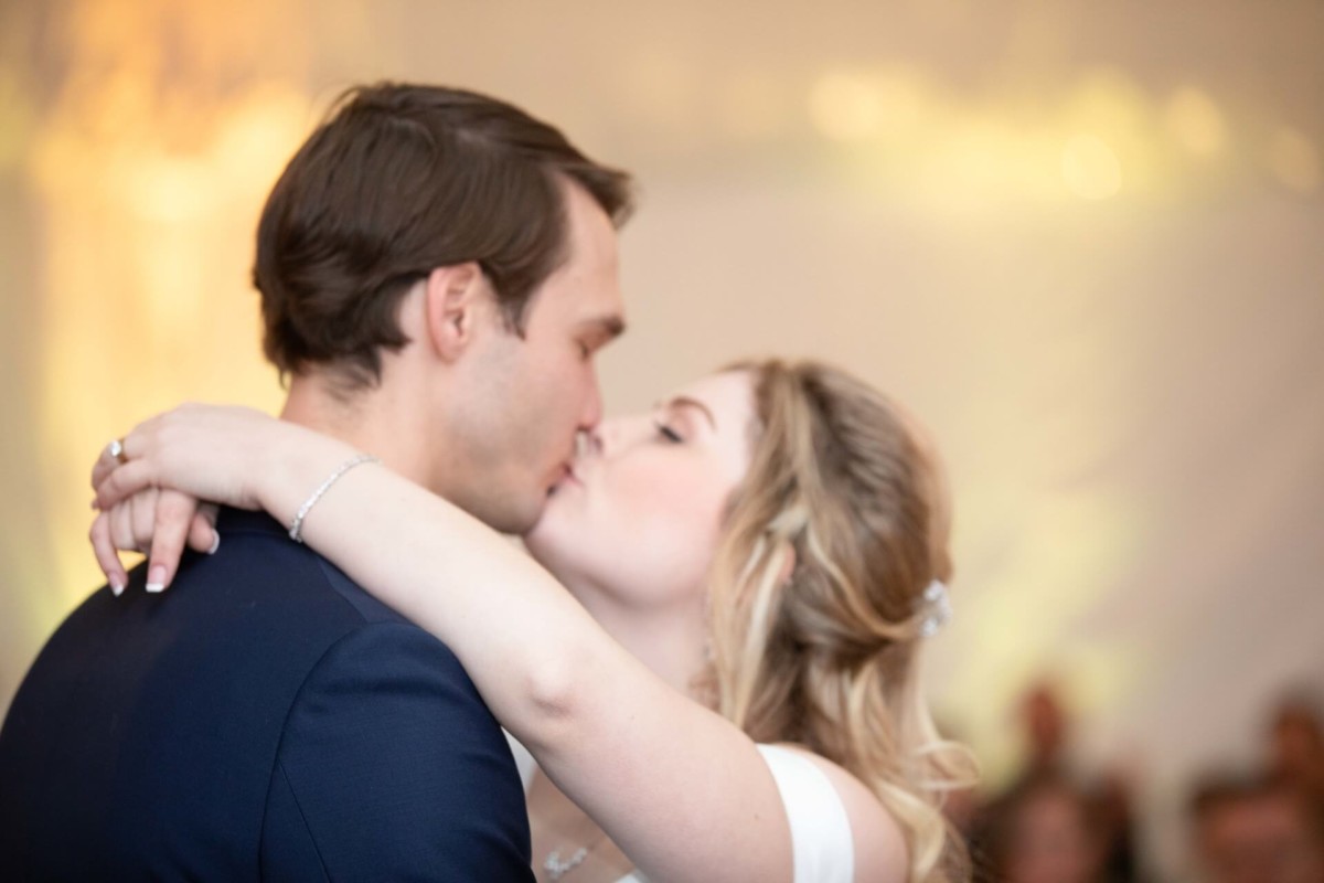 Scarlett-Michael-Wedding-Low-Res-78 - TOMMY GATZ ENTERTAINMENT A couple shares a kiss while embracing, with the background softly blurred.