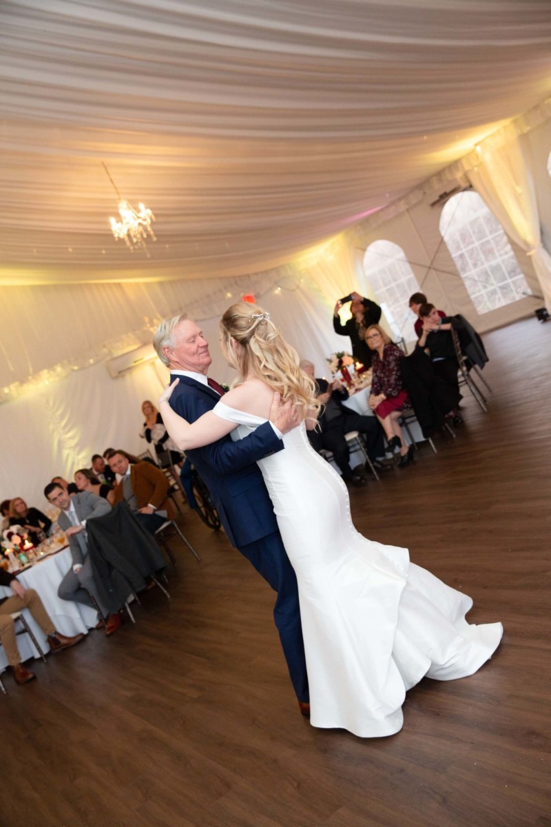Scarlett-Michael-Wedding-Low-Res-79 - TOMMY GATZ ENTERTAINMENT A bride and groom share their first dance in a decorated wedding venue, surrounded by seated guests.