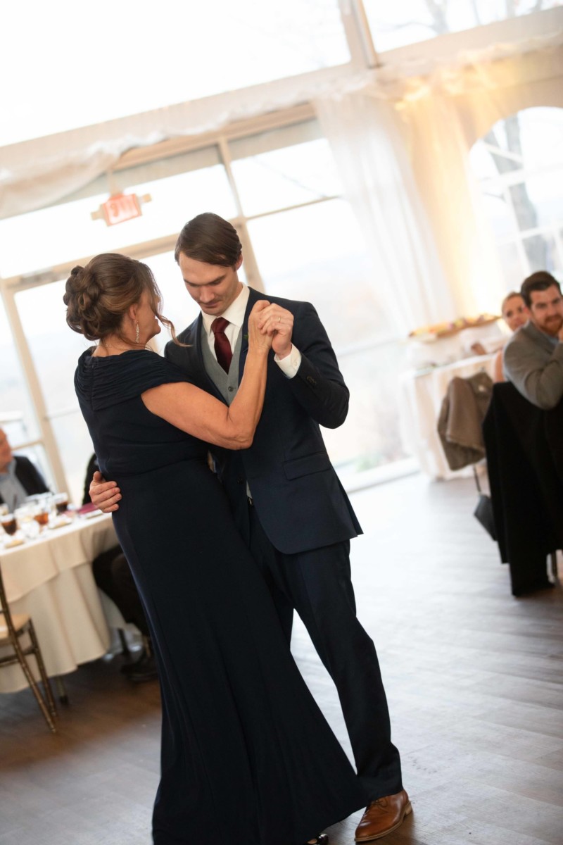 Scarlett-Michael-Wedding-Low-Res-83 - TOMMY GATZ ENTERTAINMENT A woman and a man in formal attire are dancing together in a bright room, with guests seated at tables in the background.