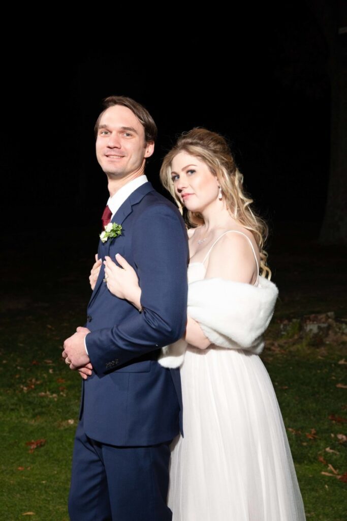 Scarlett-Michael-Wedding-Low-Res-91 - TOMMY GATZ ENTERTAINMENT A couple poses for a wedding photo outdoors at night. The bride is in a white dress, and the groom is in a dark suit.