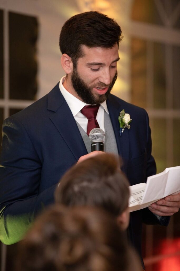 Scarlett-Michael-Wedding-Low-Res-92 - TOMMY GATZ ENTERTAINMENT A man in a suit is speaking into a microphone while holding a piece of paper.