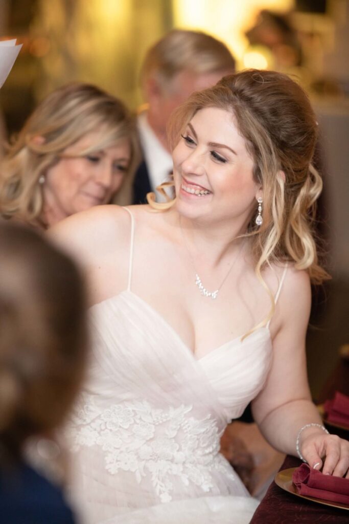 Scarlett-Michael-Wedding-Low-Res-93 - TOMMY GATZ ENTERTAINMENT A smiling bride in a white dress sits at a table surrounded by people.