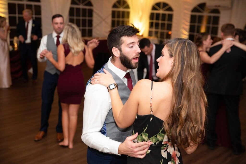 Scarlett-Michael-Wedding-Low-Res-98 - TOMMY GATZ ENTERTAINMENT A man and woman dance in a warmly lit room. Other couples are dancing in the background.
