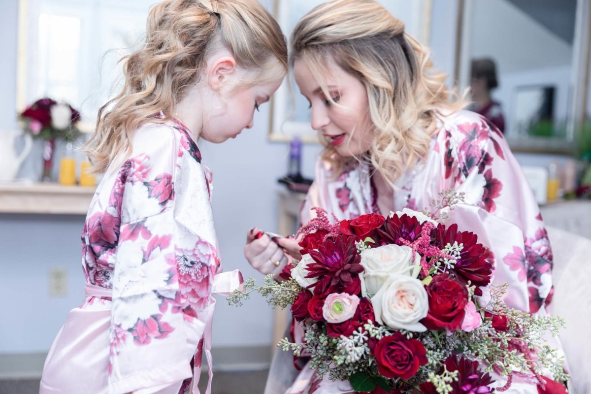 Shannon-James-Wedding-Low-Res-14 - TOMMY GATZ ENTERTAINMENT A woman in a floral robe shows a red and white bouquet to a young girl in a matching robe.