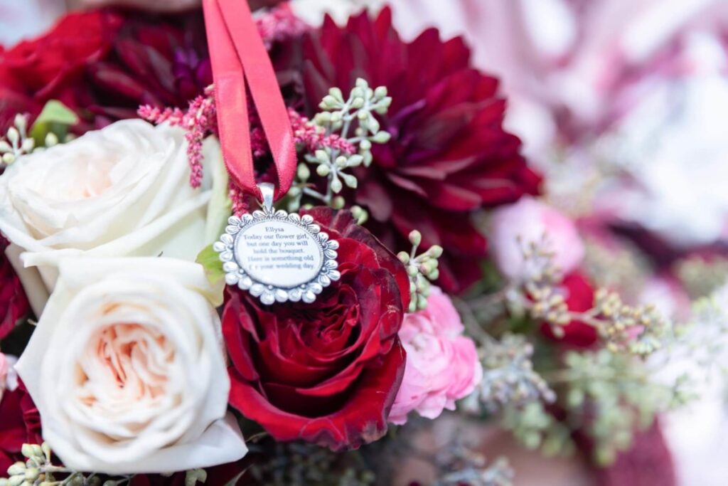 Shannon-James-Wedding-Low-Res-16 - TOMMY GATZ ENTERTAINMENT Close-up of a bouquet featuring red, pink, and white roses with a decorative pendant attached to a red ribbon.