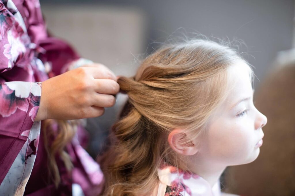 Shannon-James-Wedding-Low-Res-2 - TOMMY GATZ ENTERTAINMENT Person braiding a young girl's hair, both wearing floral-patterned robes.