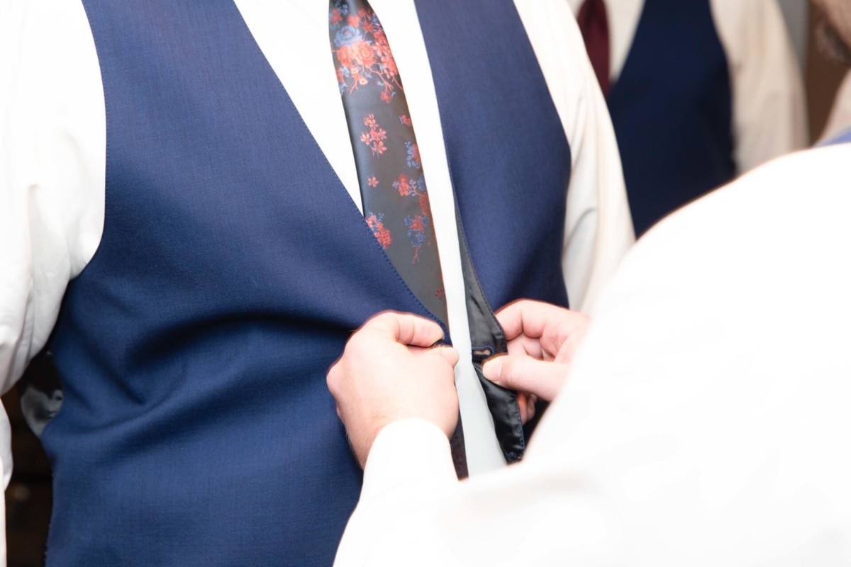 Shannon-James-Wedding-Low-Res-25 - TOMMY GATZ ENTERTAINMENT Person in a blue vest adjusts another person's floral tie.