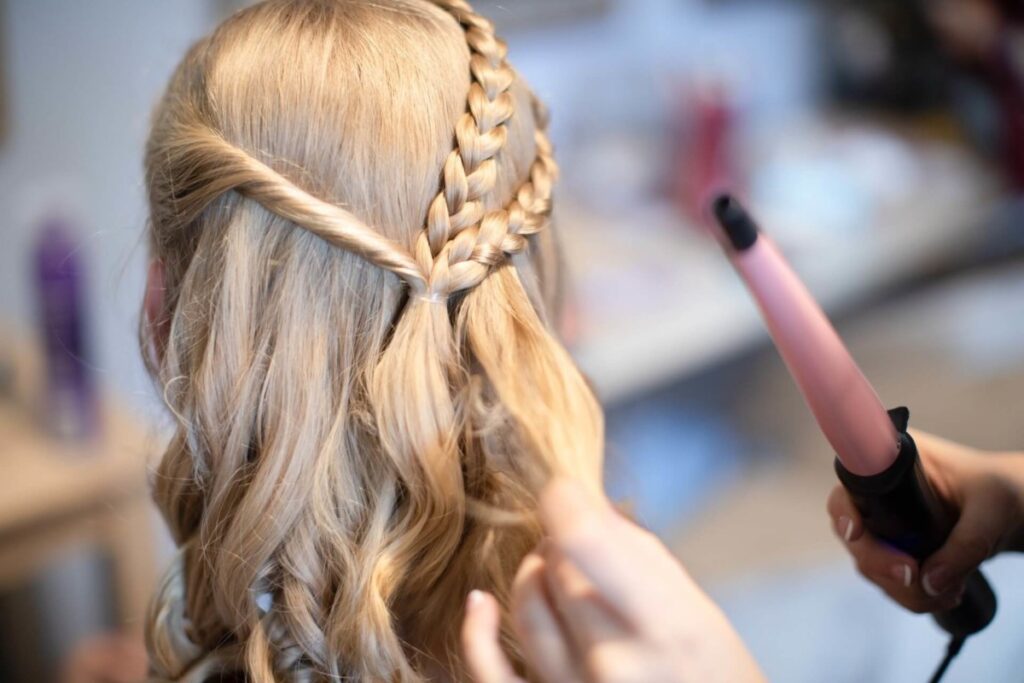 Shannon-James-Wedding-Low-Res-3 - TOMMY GATZ ENTERTAINMENT A person with long, blond hair styled in braids and curls is having their hair curled with a curling wand in a salon setting.