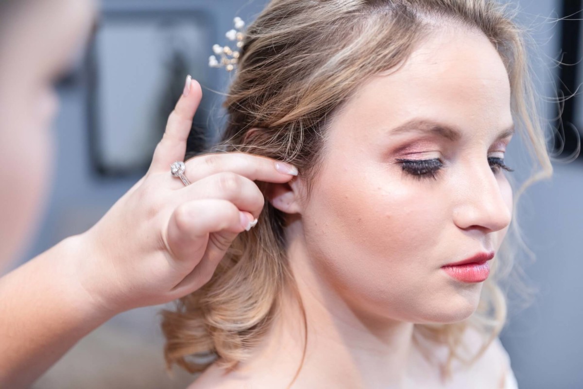 Shannon-James-Wedding-Low-Res-36 - TOMMY GATZ ENTERTAINMENT A woman with makeup is getting her hair adjusted by another person indoors.