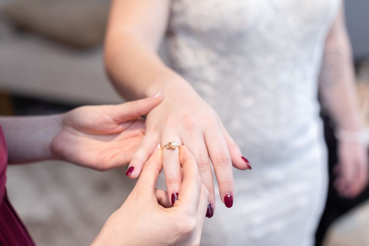 Shannon-James-Wedding-Low-Res-38 - TOMMY GATZ ENTERTAINMENT A person places a gold ring on another person's finger, who is wearing a white dress.