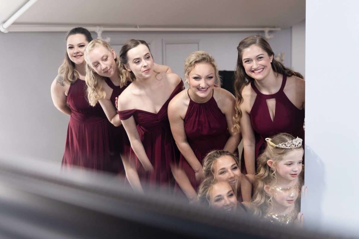 Shannon-James-Wedding-Low-Res-45 - TOMMY GATZ ENTERTAINMENT A group of women and children in party dresses smiling and looking in one direction indoors.