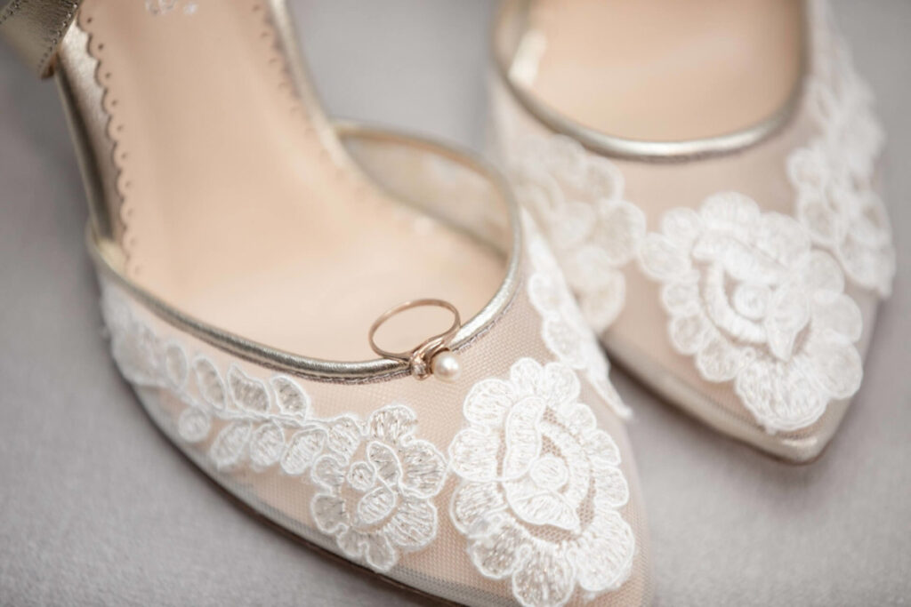 Shannon-James-Wedding-Low-Res-8 - TOMMY GATZ ENTERTAINMENT A pair of lace-decorated shoes with a ring placed on one of them.