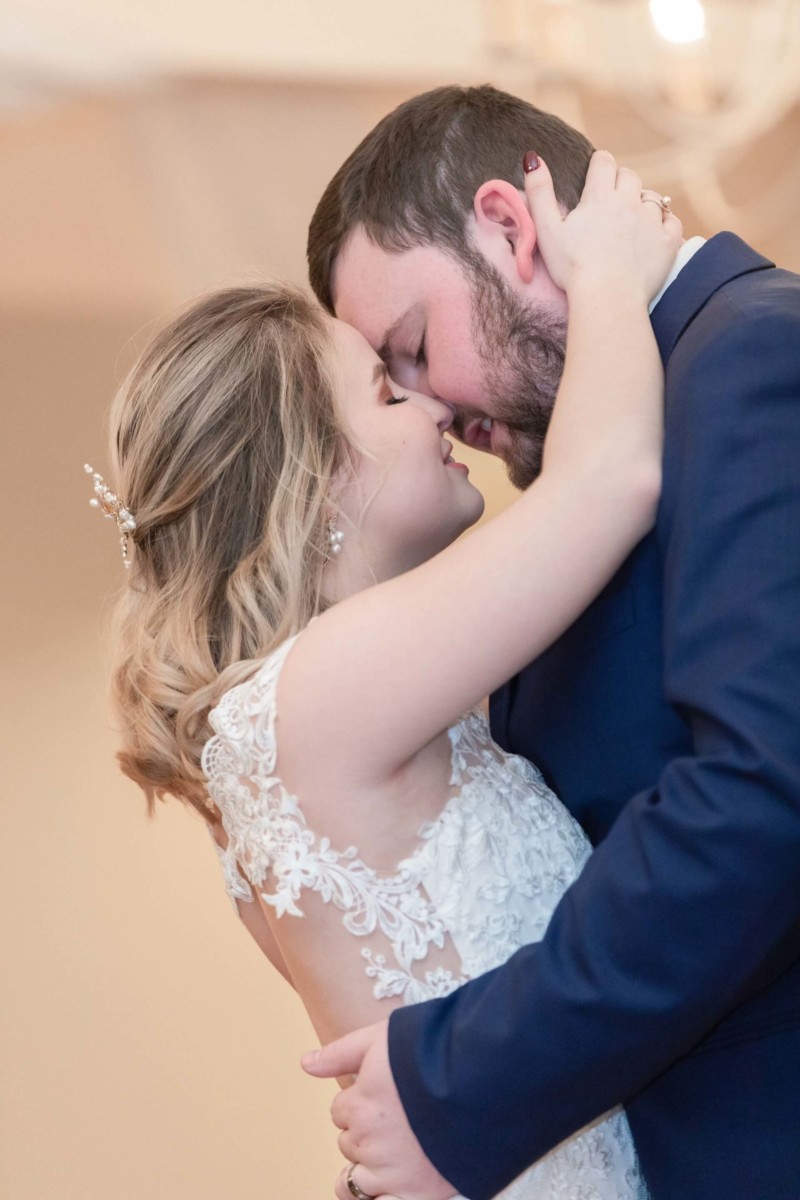 Shannon-James-Wedding-Low-Res-81 - TOMMY GATZ ENTERTAINMENT A couple in wedding attire shares an intimate embrace and kiss. The bride wears a lace dress, and the groom is in a dark suit.