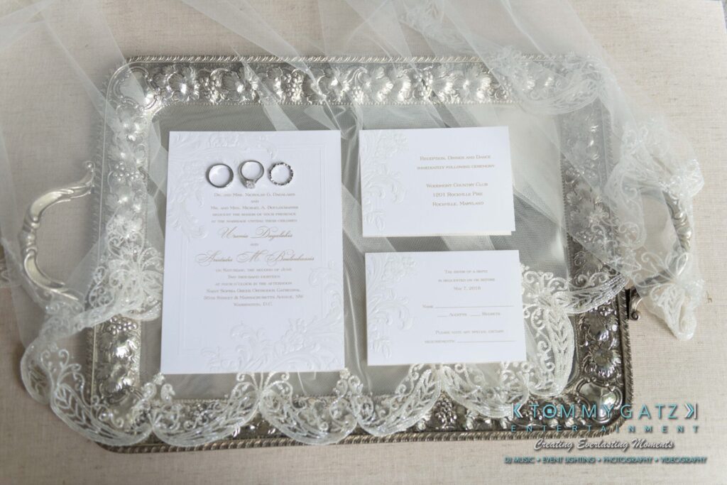 Elegant wedding invitations and three rings displayed on a silver tray with lace trim.