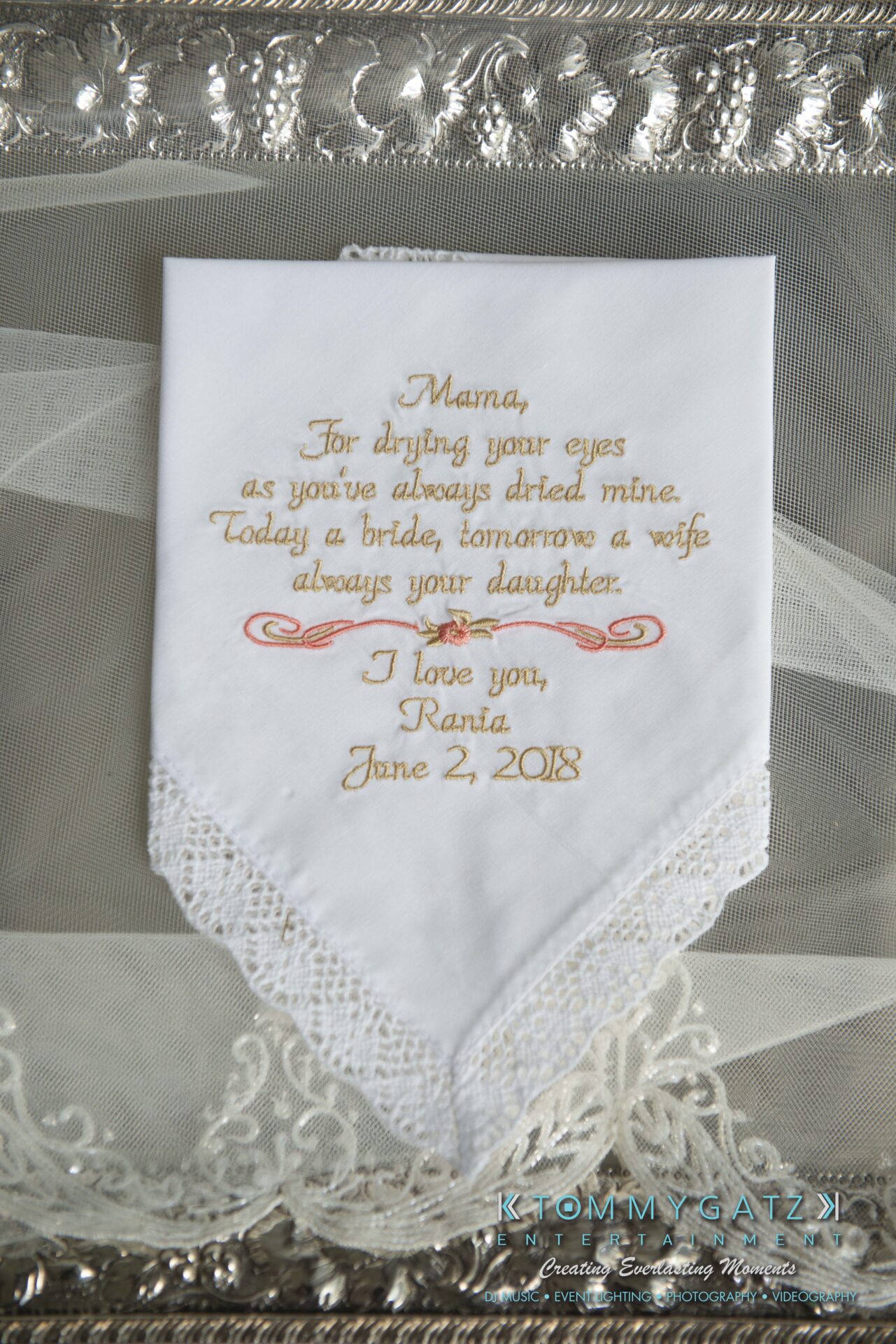 Urania-Aristidis-060218-PREP-Low-Res-WM-26 - TOMMY GATZ ENTERTAINMENT A lace-trimmed handkerchief with embroidered text expressing love from a daughter to her mother, dated June 2, 2018, placed on a decorative surface.