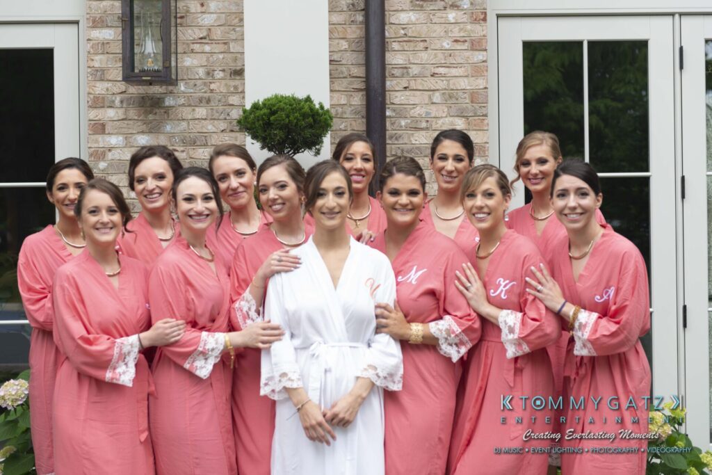 Group of women in matching pink robes pose with a woman in a white robe in front of a brick building.