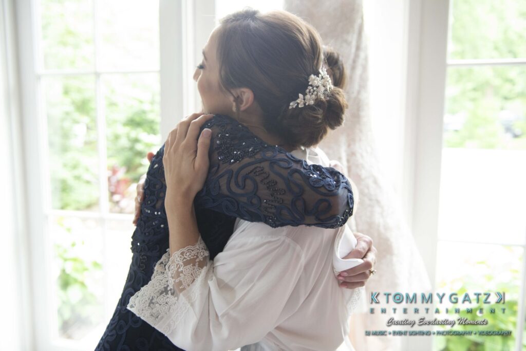 Two people embracing in front of a bright window, one in white, the other in dark clothing with lace details.