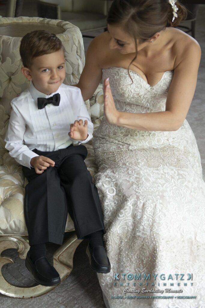 Urania-Aristidis-060218-PREP-Low-Res-WM-64 - TOMMY GATZ ENTERTAINMENT A bride playfully gestures to a young boy in a suit sitting beside her on an ornate chair.