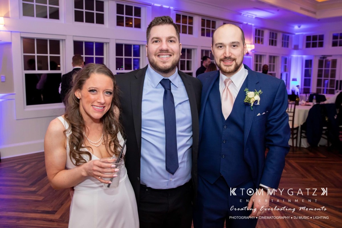 BrittanyDaniel-WEDDING-Highlights-107 - TOMMY GATZ ENTERTAINMENT Three people pose together at an indoor event. The woman on the left holds a drink, while both men on the right wear suits.
