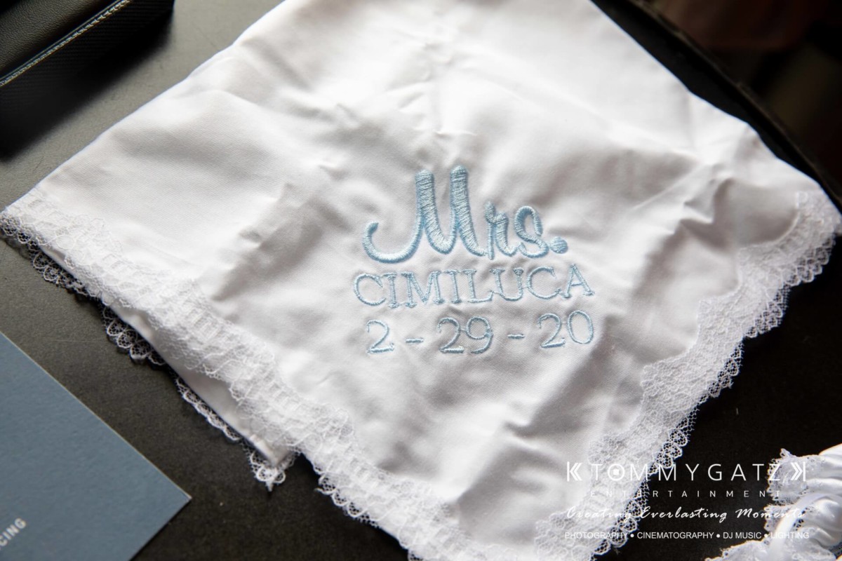 BrittanyDaniel-WEDDING-Highlights-11 - TOMMY GATZ ENTERTAINMENT White handkerchief with lace edges, embroidered with "Mrs. Cimilluca 2-29-20" in blue thread.