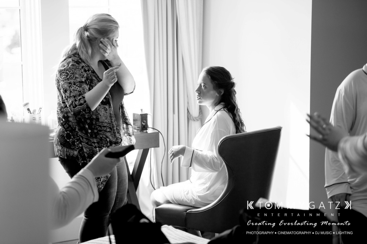BrittanyDaniel-WEDDING-Highlights-31 - TOMMY GATZ ENTERTAINMENT A bride sits in a chair, getting ready as a stylist stands nearby. Another person is partially visible in the foreground.