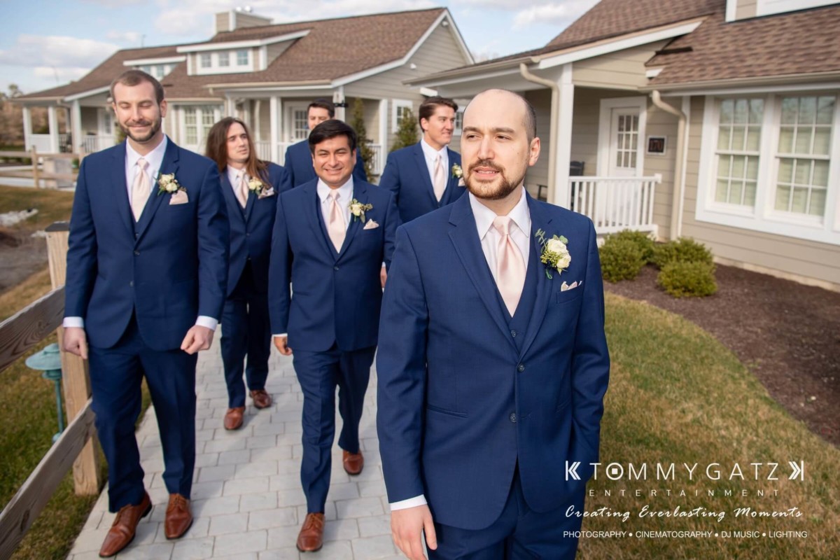 BrittanyDaniel-WEDDING-Highlights-43 - TOMMY GATZ ENTERTAINMENT A group of six men in blue suits walk on a path outside a house.