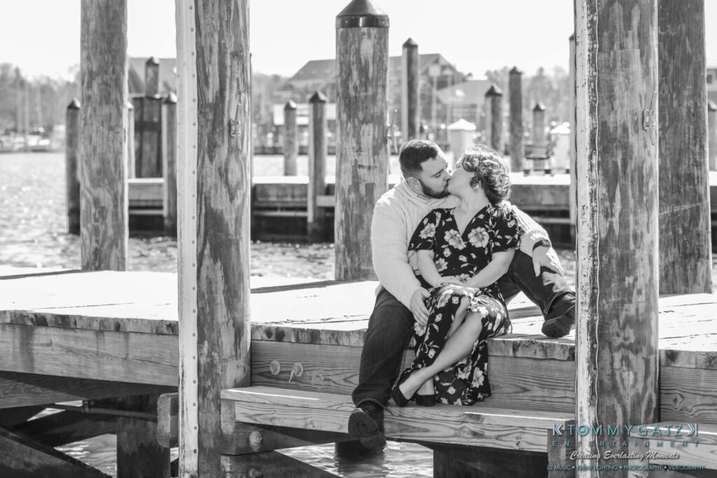 Shannon-James-031319-FINALS-Low-Res-WM-20 - TOMMY GATZ ENTERTAINMENT A couple sits on a wooden dock, kissing, with boats and water in the background.