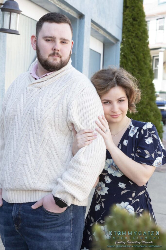 Shannon-James-031319-FINALS-Low-Res-WM-6 - TOMMY GATZ ENTERTAINMENT A man in a white sweater and jeans stands next to a woman in a floral dress, who is leaning on his arm outside a building.