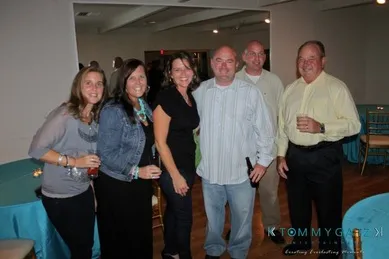 A group of six people standing together in a room with tables, smiling at the camera.