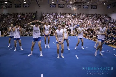 A group of people in matching outfits perform a routine on a gym floor in front of a large seated audience.