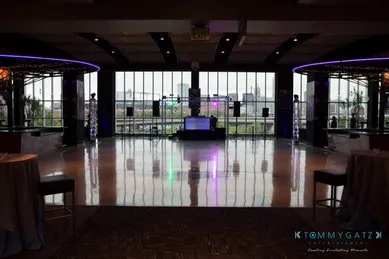 Spacious event venue with large windows, circular light fixtures, a dance floor, and a DJ setup.